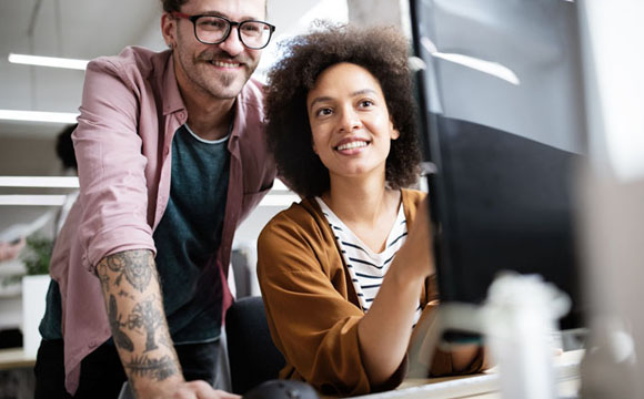 jóvenes sonrientes en una oficina mirando una pantalla